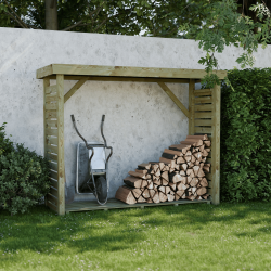 Abri-bûches DALLAS XL en ambiance dans un jardin, contre un mur avec des bûches et une brouette entreposées à l'intérieur